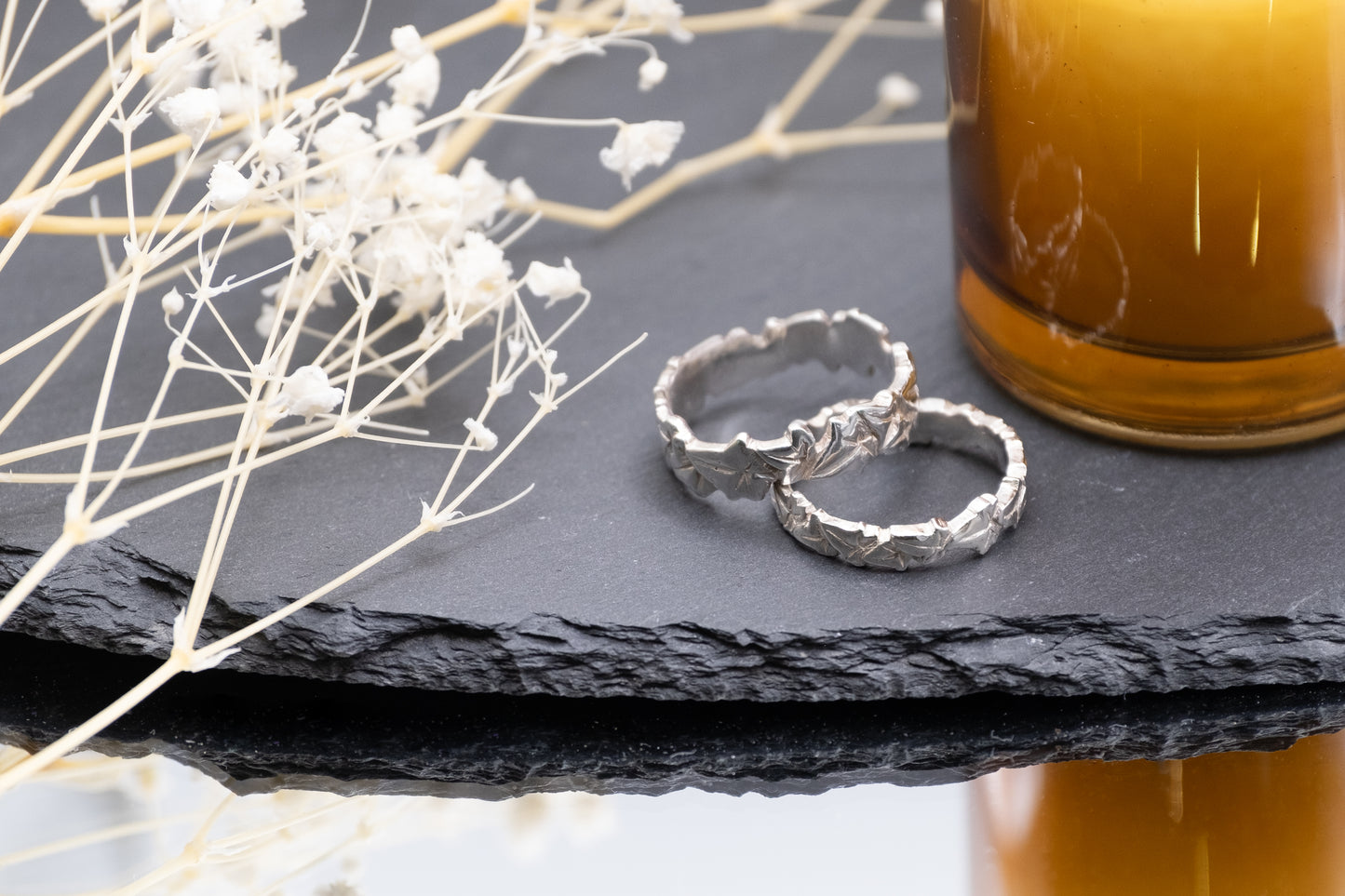 two silver ivy leaf rings of different widths on a slate with flowers and a candle