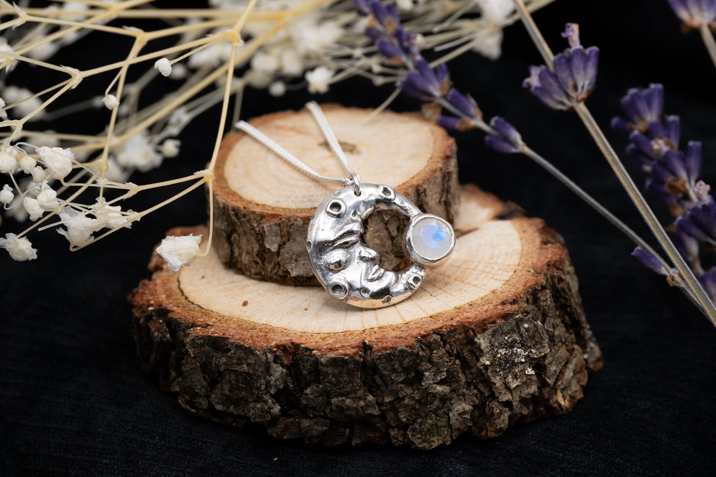 a silver man in the moon pendant with a moonstone on wood with flowers