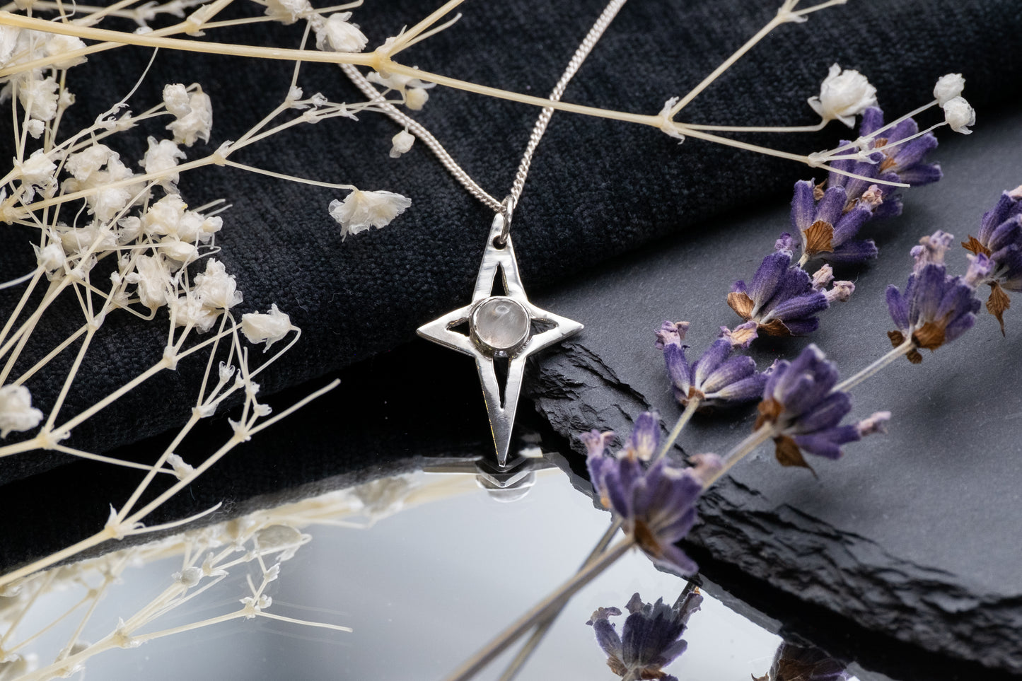 a silver star shaped pendant with a moonstone on a mirror with a slate and flowers