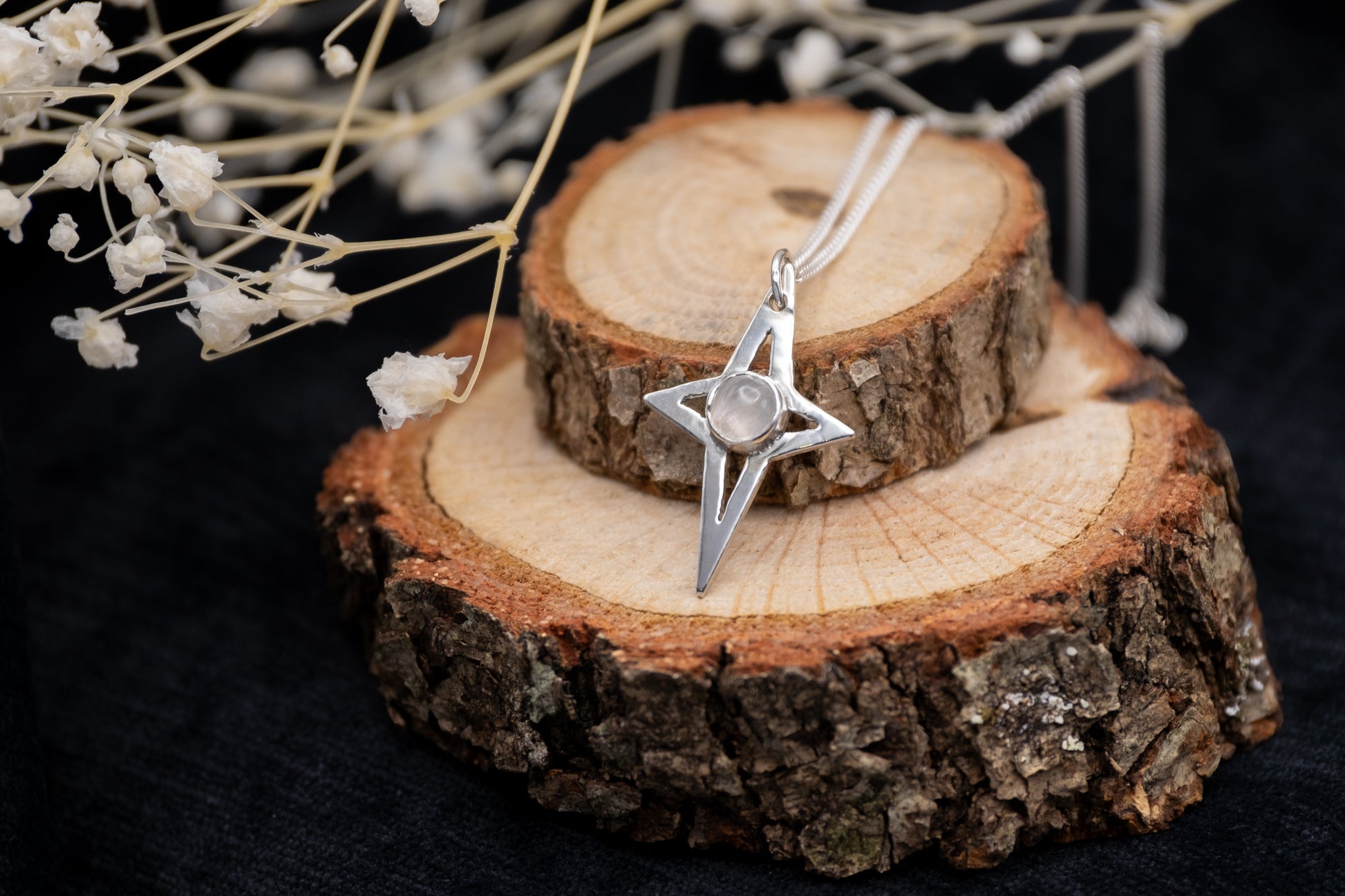 a silver star shaped pendant with a moon stone on wood