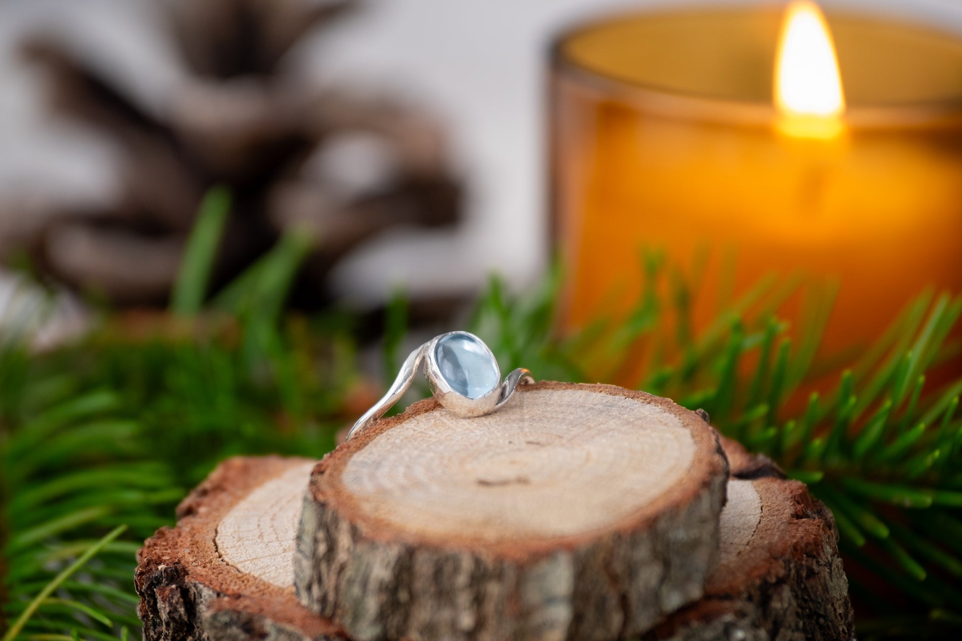 a festive photo of a silver topaz ring surrounded by pine needles, pine cones and a candle