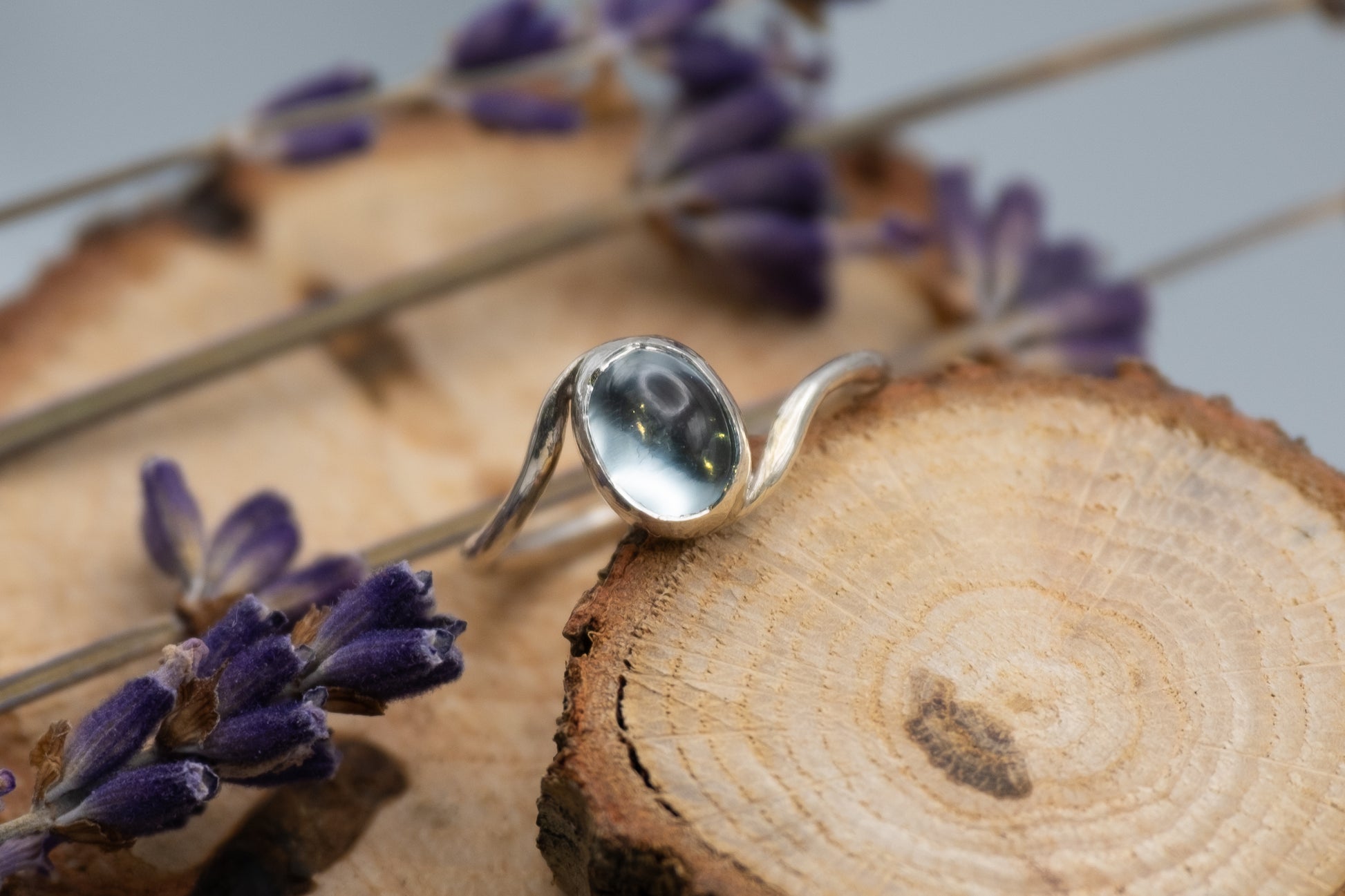 a silver topaz ring with a wave design on wood slices with flowers