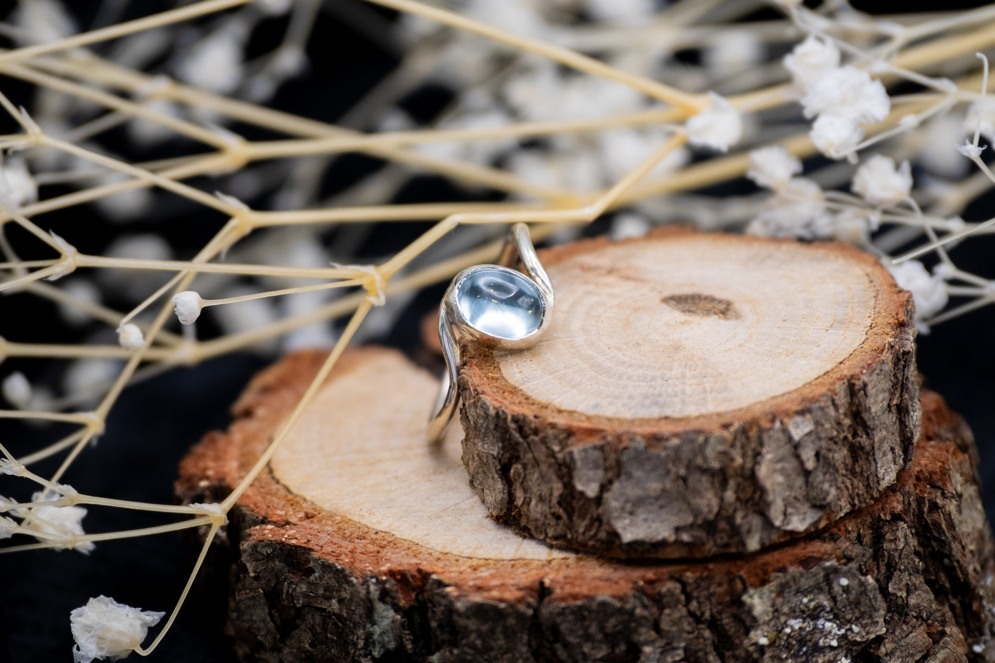 a silver topaz wave design ring on wood with flowers