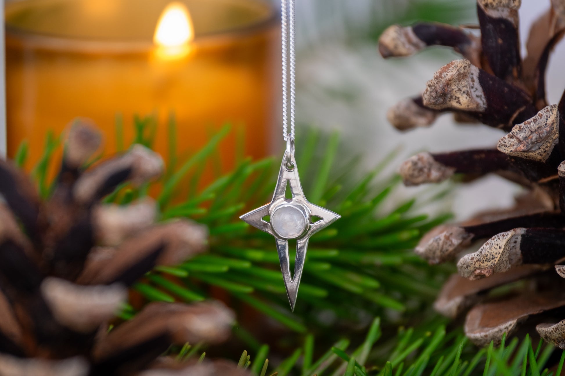 a festive photo of a star shaped silver pendant surrounded by pine needles, pine cones and a candle